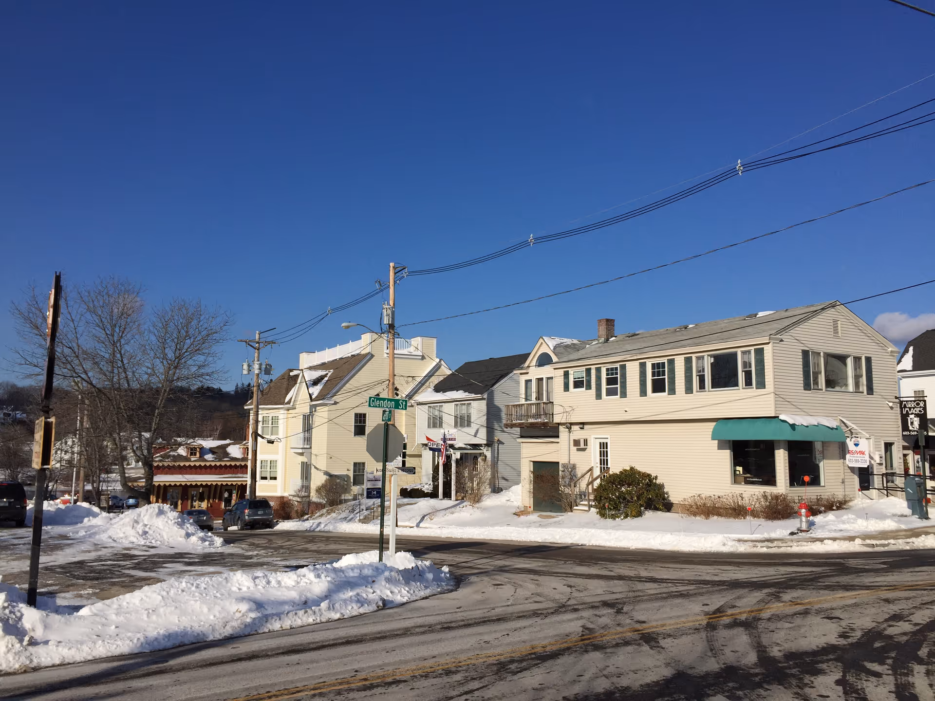 Snowy small-town street with beige houses, power lines, and a green awning.