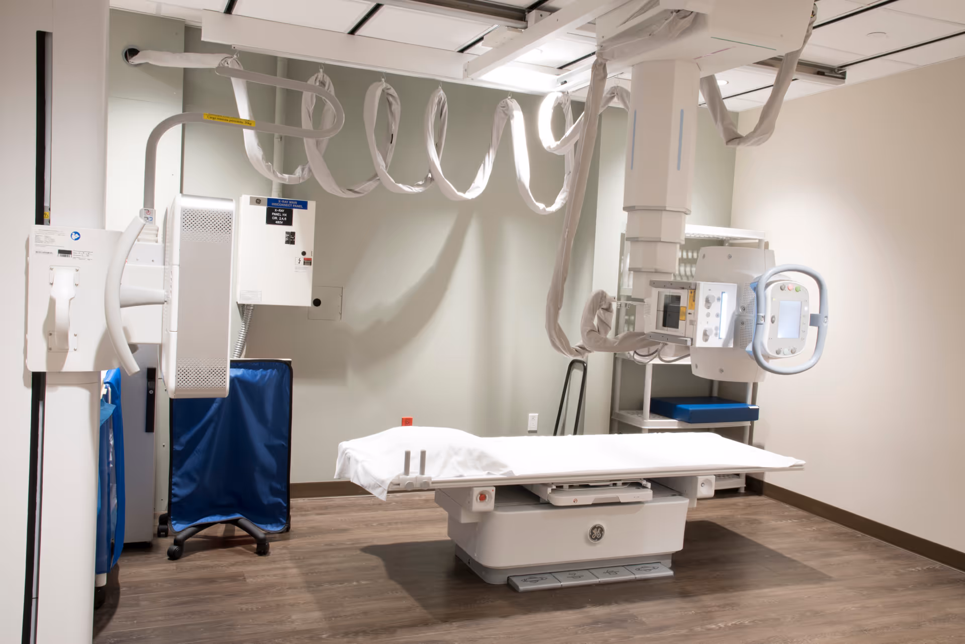 Hospital X-ray imaging room with a flat table and overhead scanning gantry.