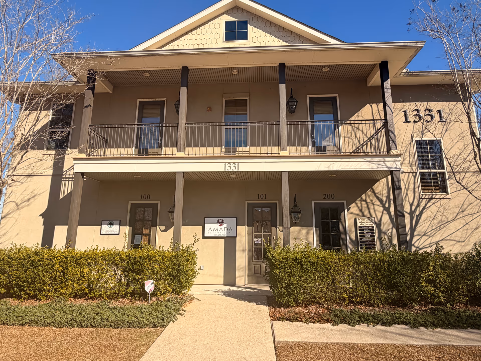 Front exterior of Amada Senior Care building with balcony, doors, and shrubs.