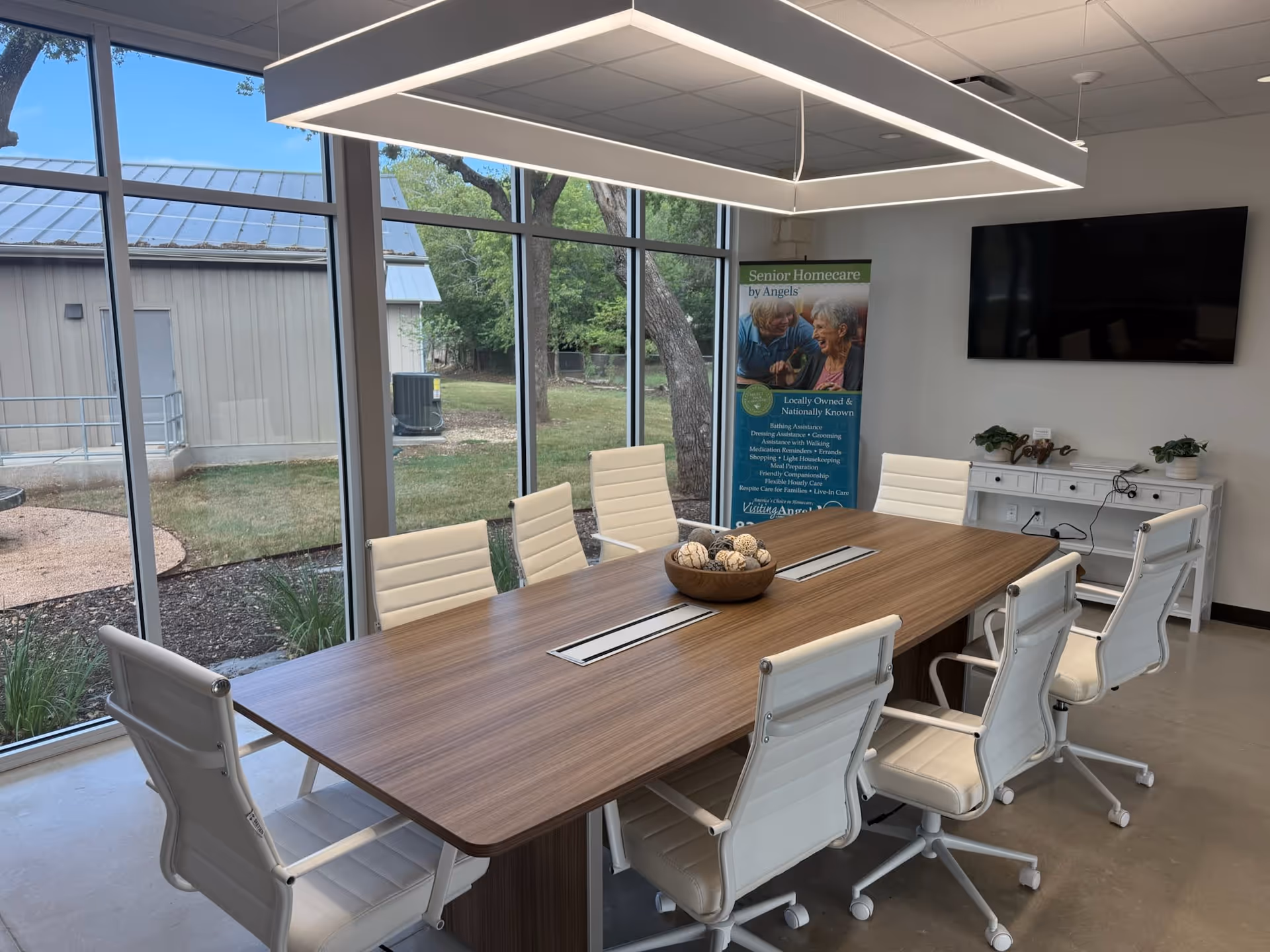 Bright conference room with a long wooden table and white chairs by large windows.