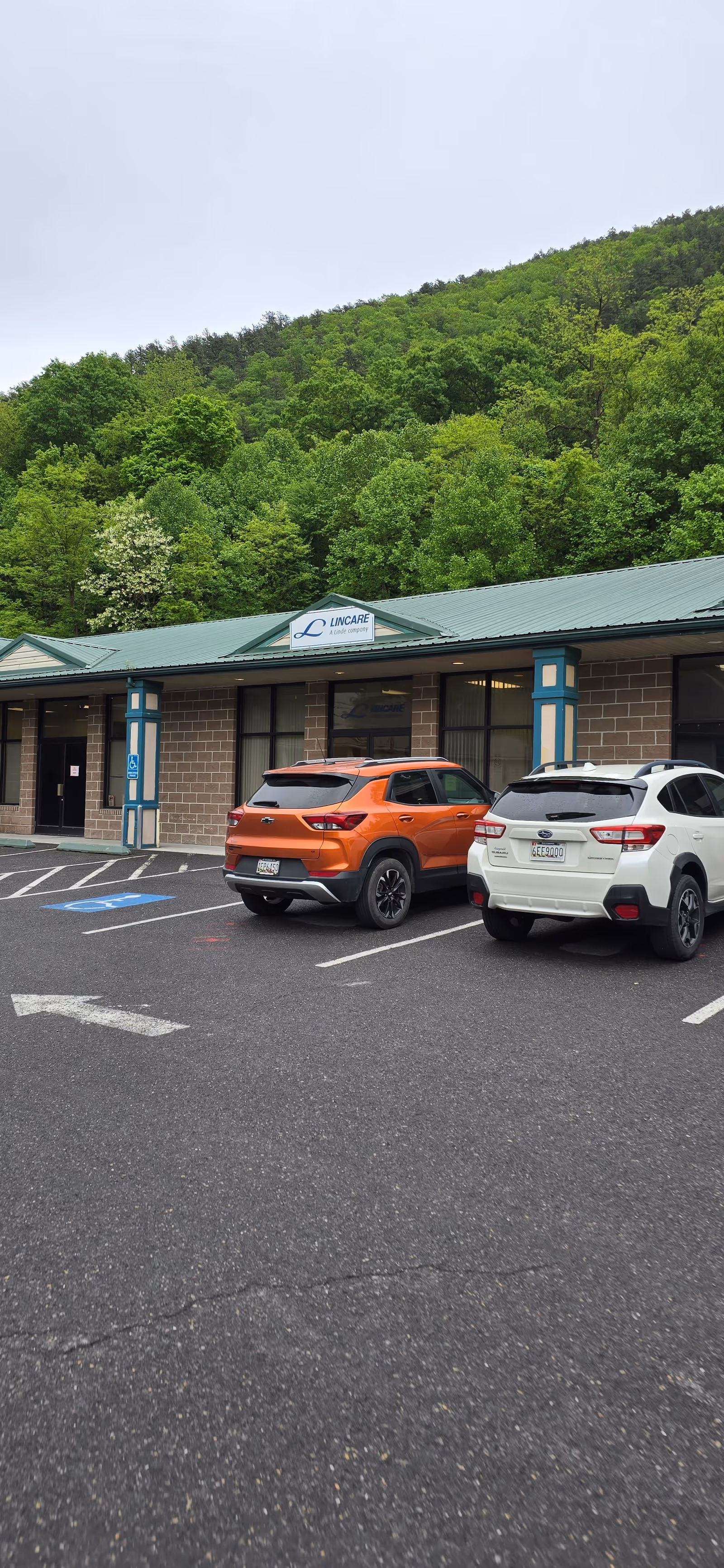 Exterior view of a Lincare facility with parked cars and a wooded hillside behind