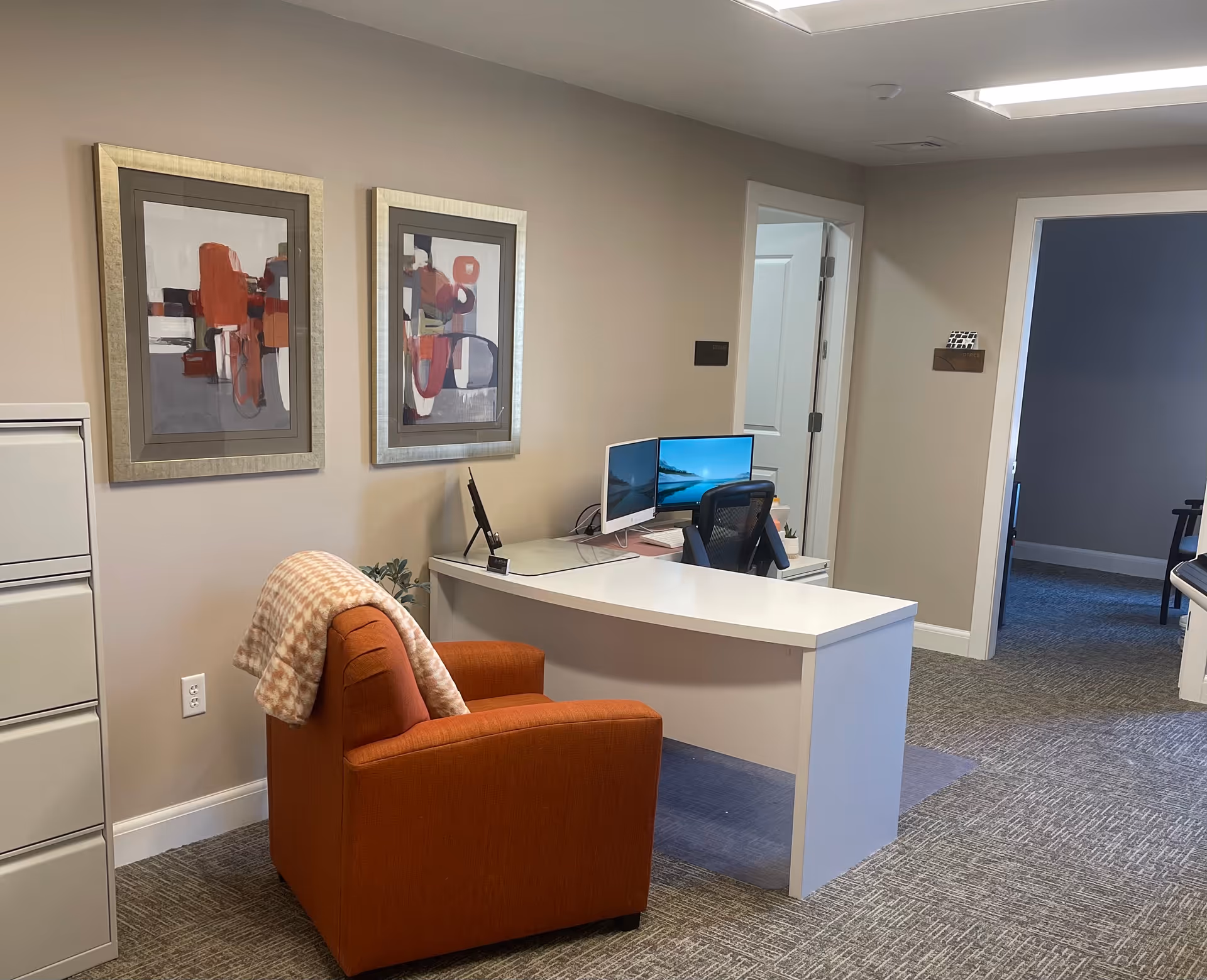 Orange chair at a white reception desk in a neutral office with framed abstract art.