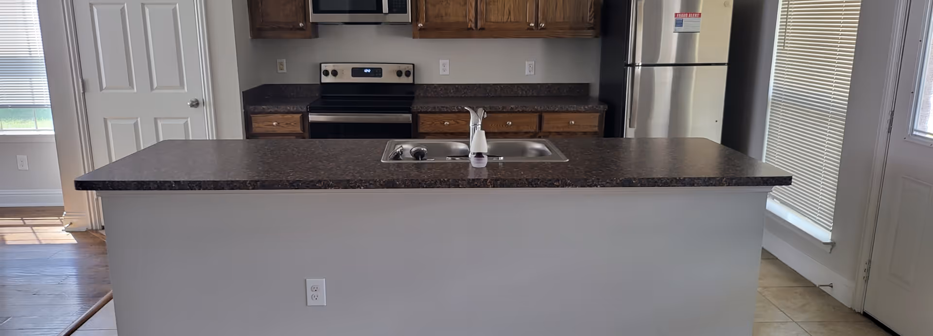 A modern kitchen with an island, sink, stove, cabinets, and a refrigerator.