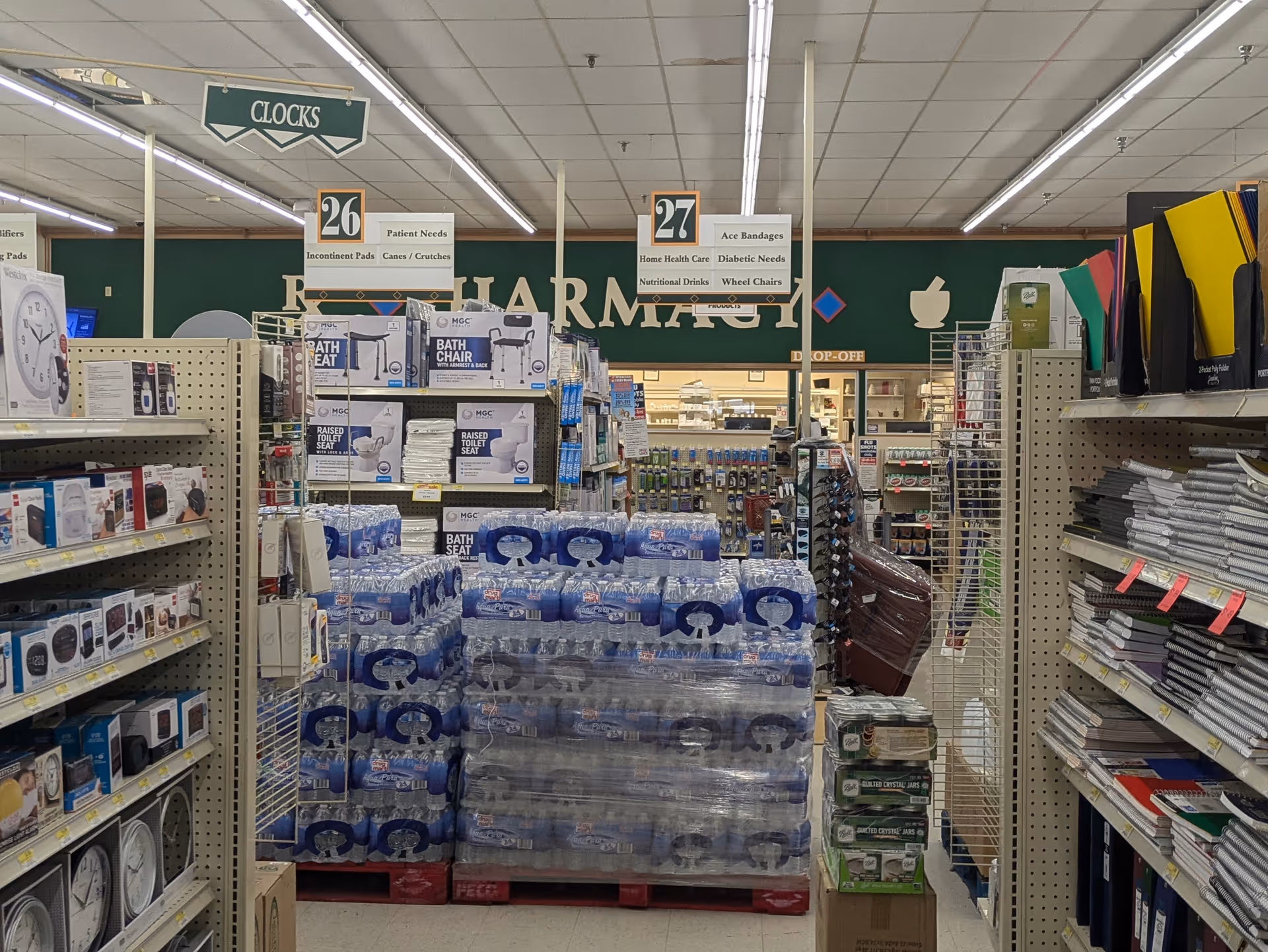 Inside Discount Drug Mart, pharmacy aisle with shelves, signage, and bulk water pallets.