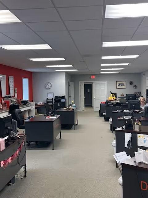 Office with multiple desks, computers, and staff in a busy administrative area.