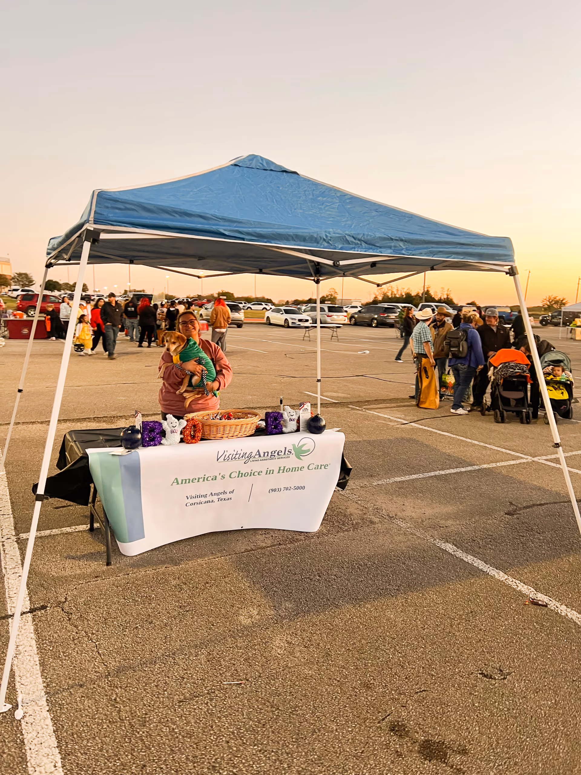 A blue canopy tent shelters a promotional table at an outdoor parking lot event.