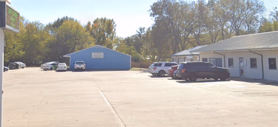Wide exterior view of a senior care facility with a parking lot and blue buildings.