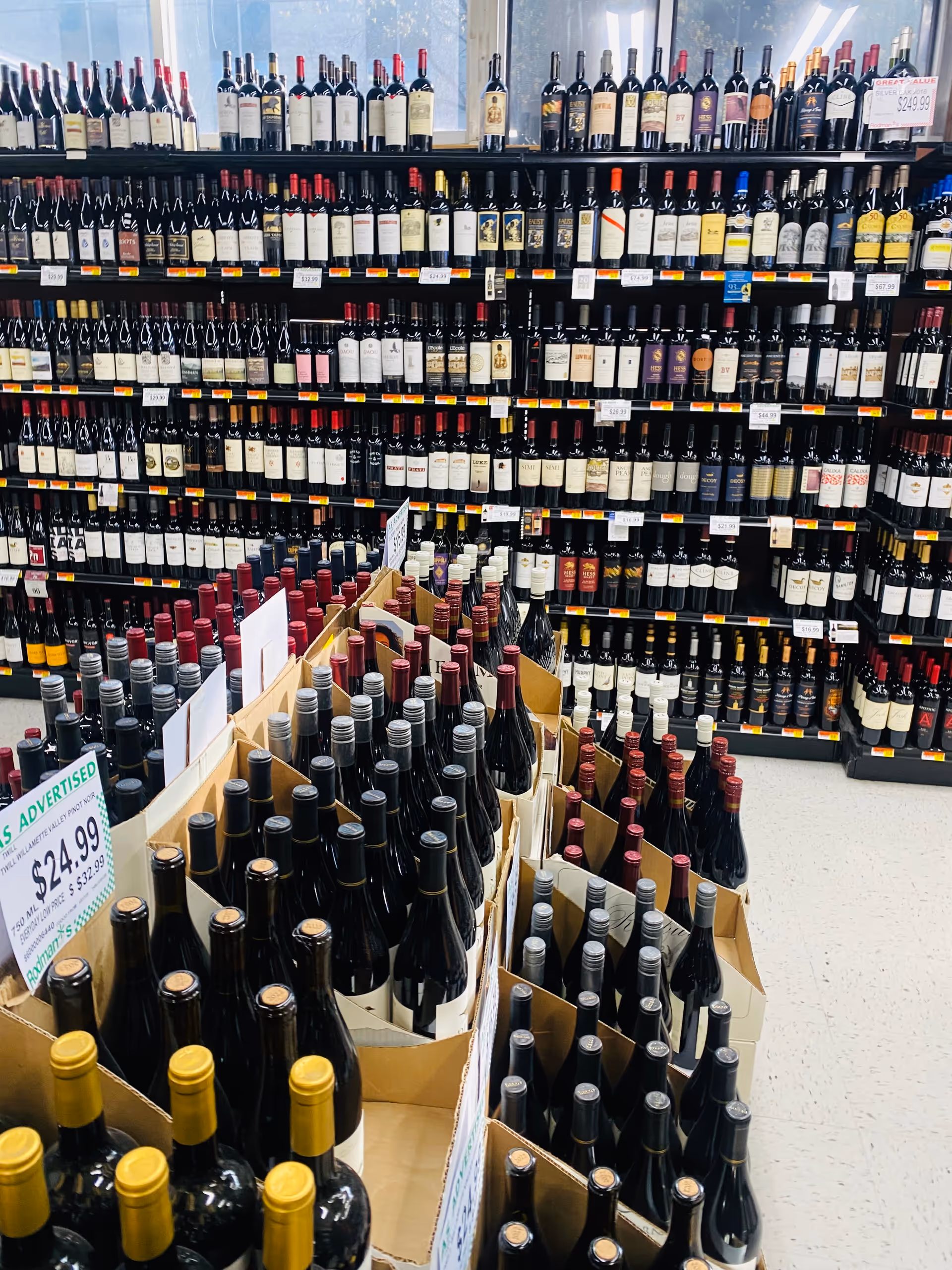 Rows of wine bottles line shelves in a well-lit store aisle.