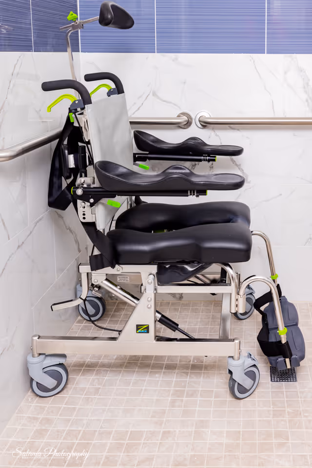 Mobility transfer chair on wheels in a tiled bathroom with grab bars.