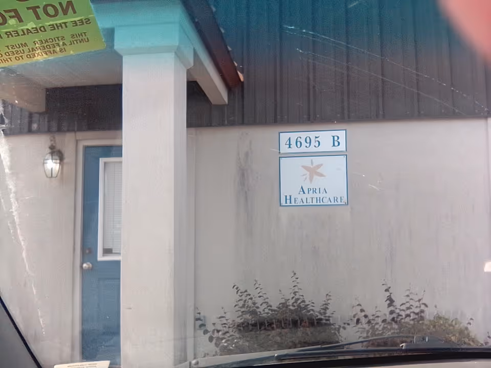 Exterior view of a facility entrance with a blue door, pillar, and Apria Healthcare sign.