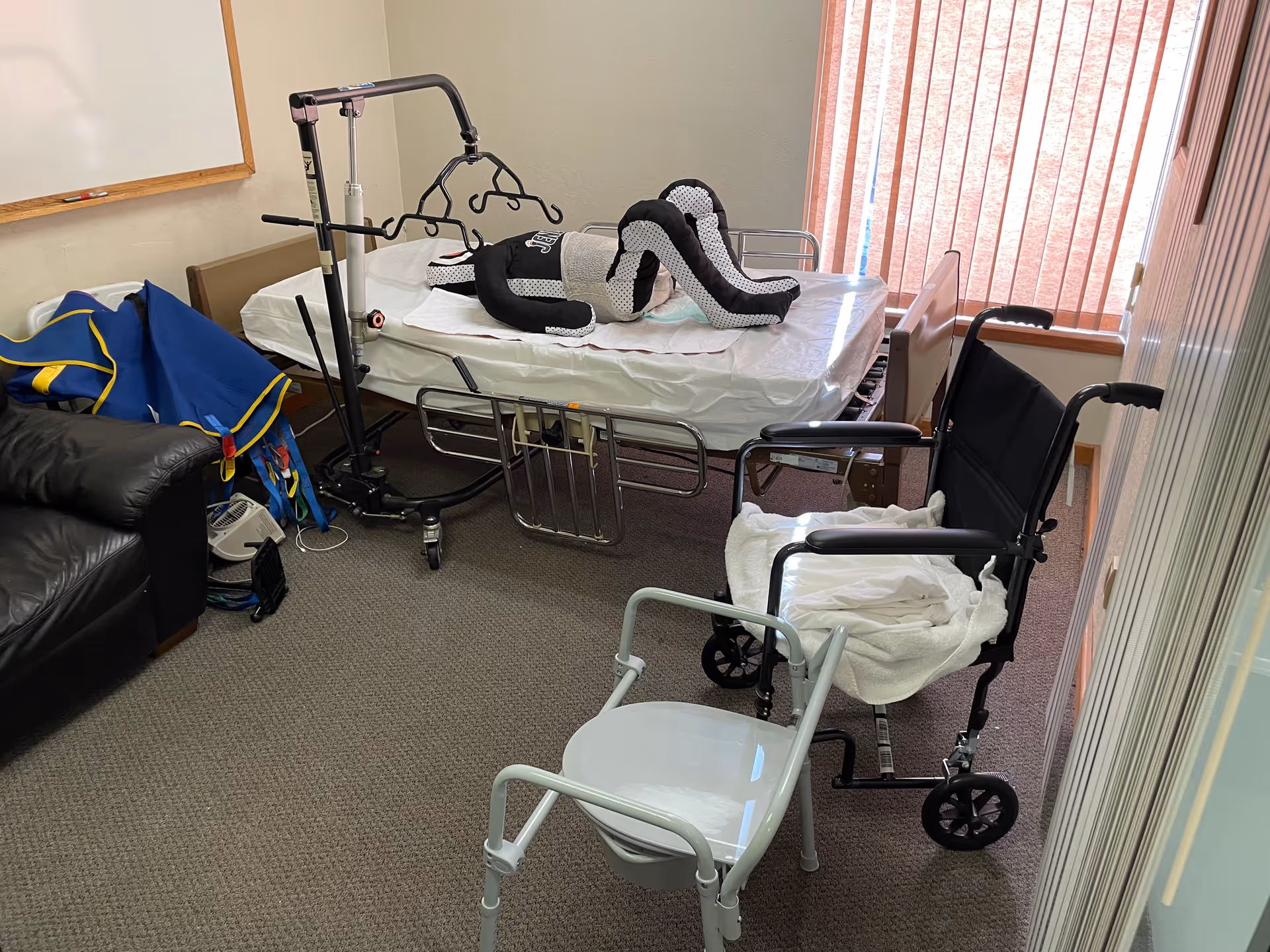 Hospital-style patient room with bed, mobility aids, and chairs.