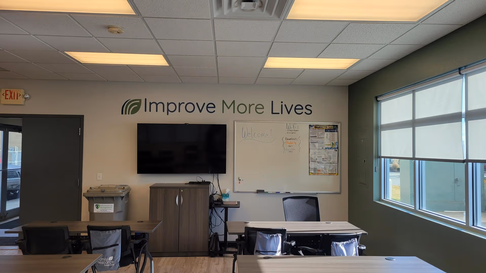 A conference room in a care facility with a sign, whiteboard, TV, and tables.
