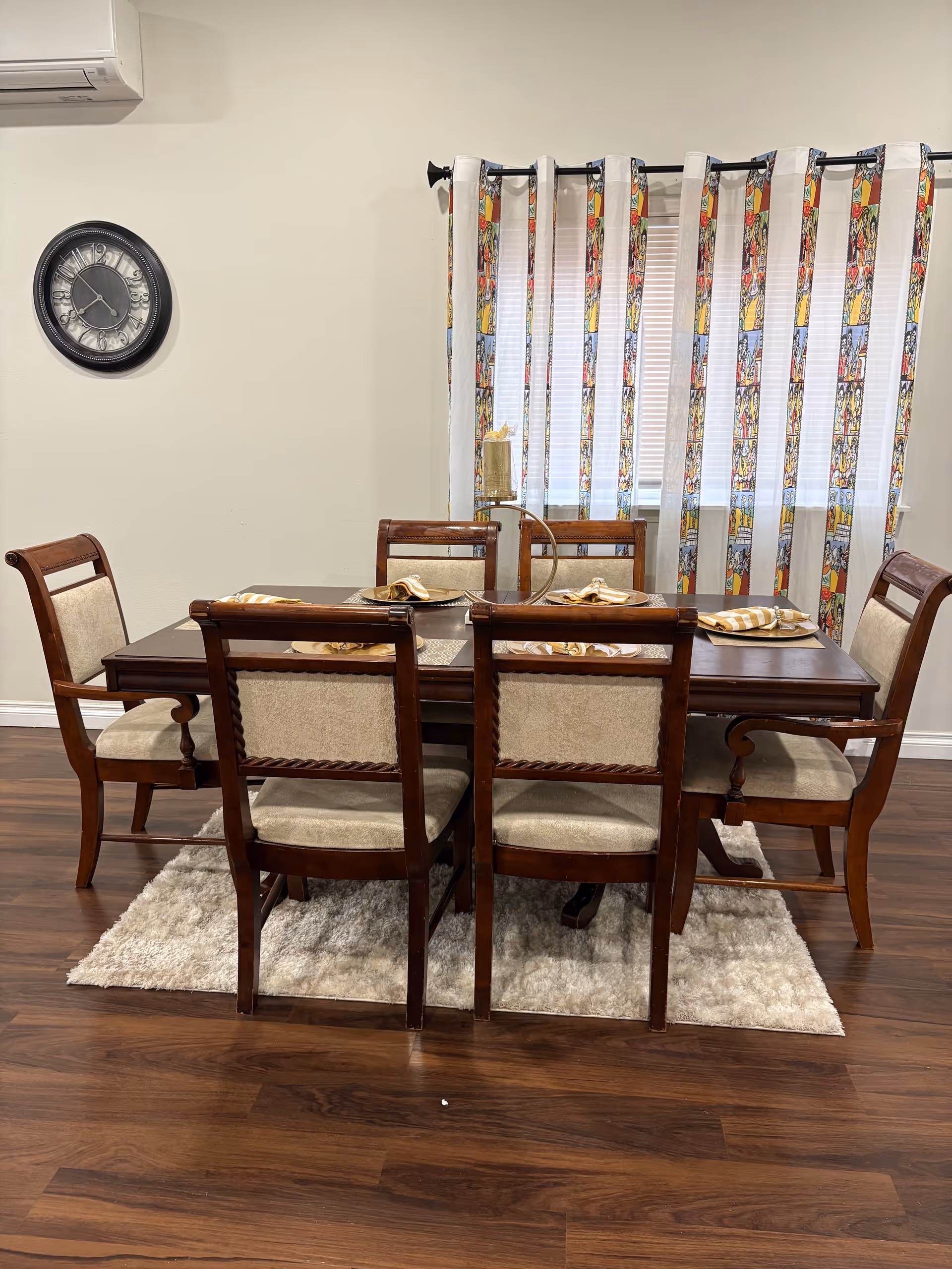 Six wooden chairs surround a dining table in a dining room with curtains.