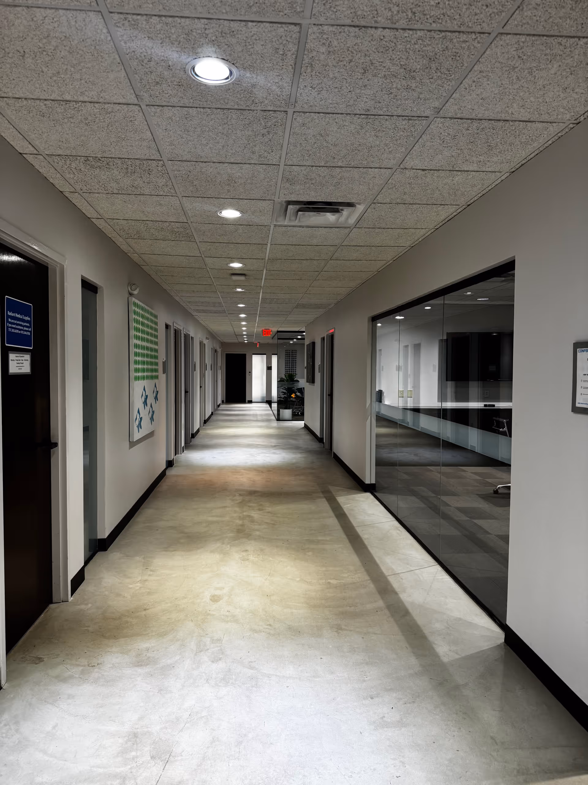 Long, lit hallway in a senior living facility with doors and a glass-walled room.