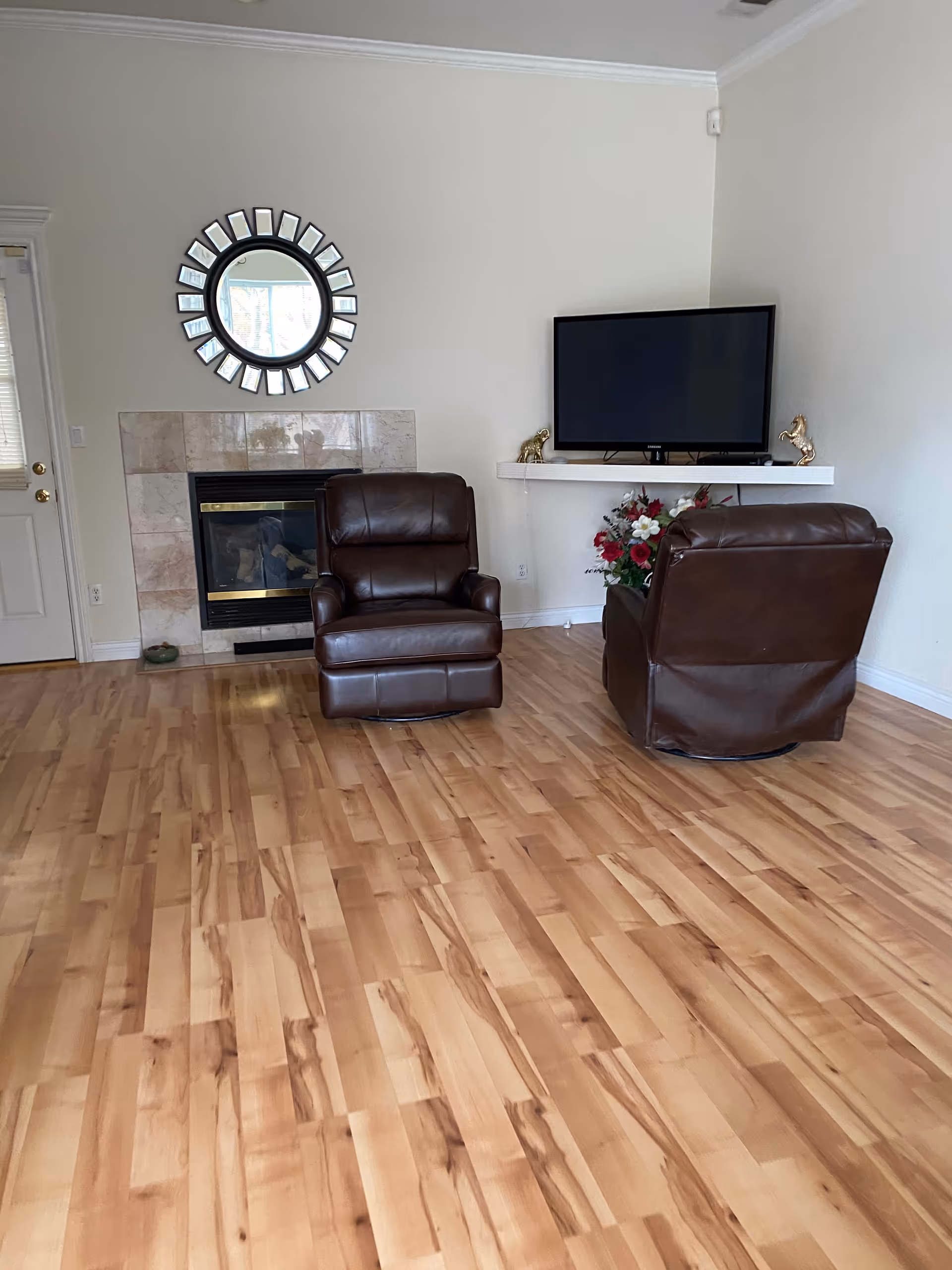 Cozy living room with two brown leather chairs, a fireplace, TV, and round mirror.