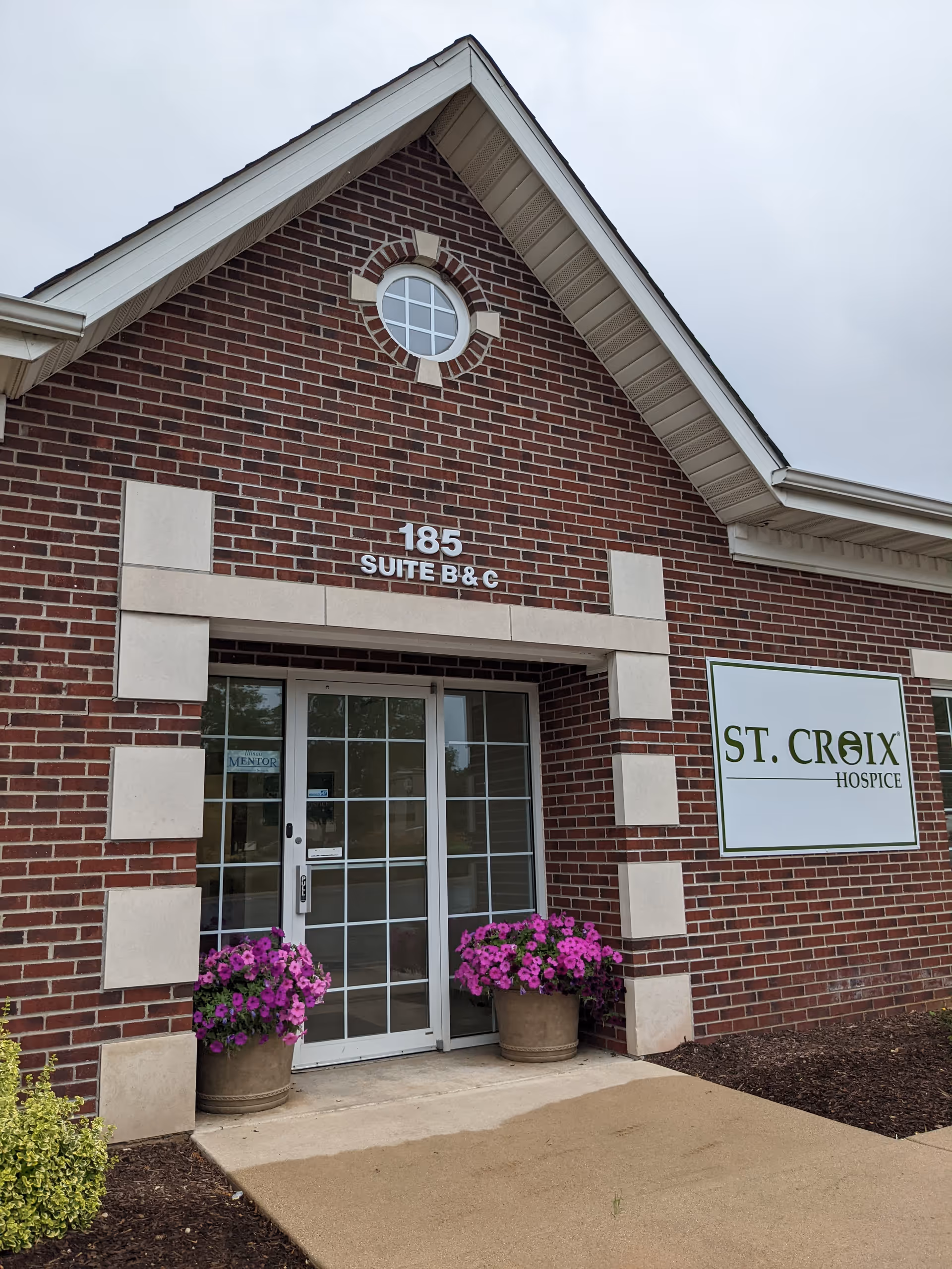The brick exterior of St. Croix Hospice with glass doors and potted flowers.