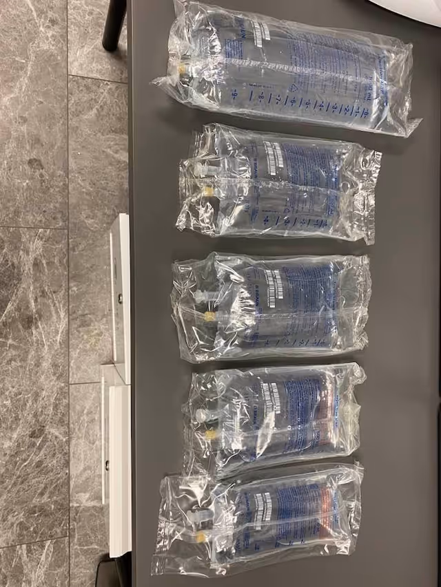 Six sealed clear IV fluid bags laid on a gray table.