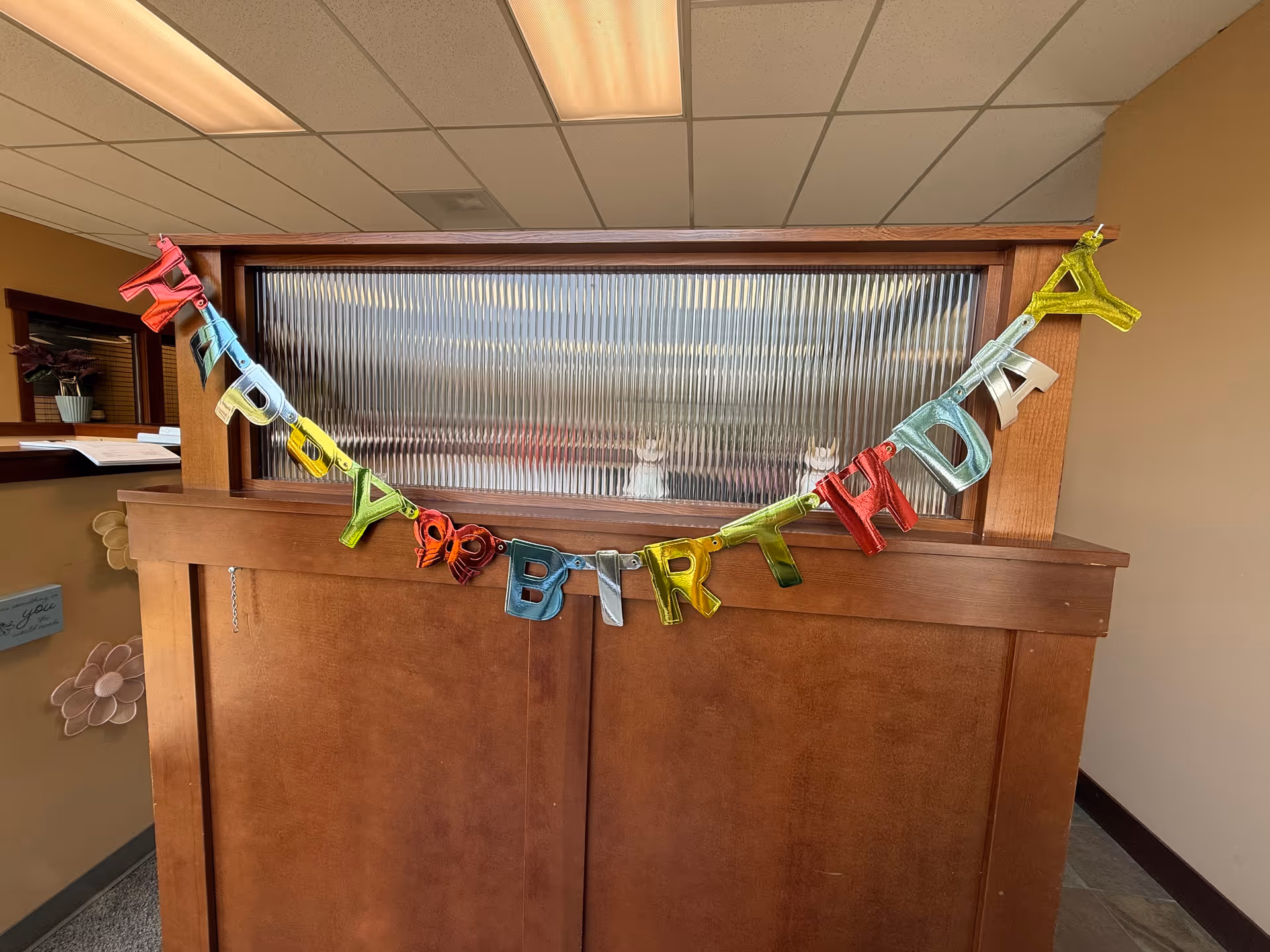 Wooden reception desk with frosted glass window and a colorful birthday banner.