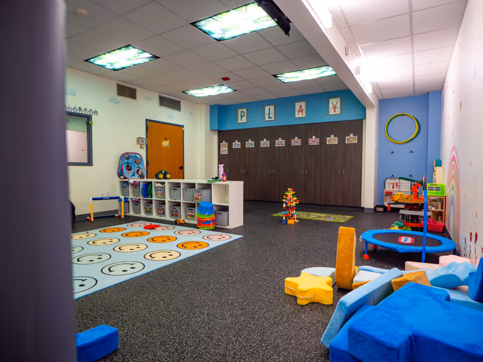 Bright children's playroom with shelves, foam blocks, toys, and colorful mats.