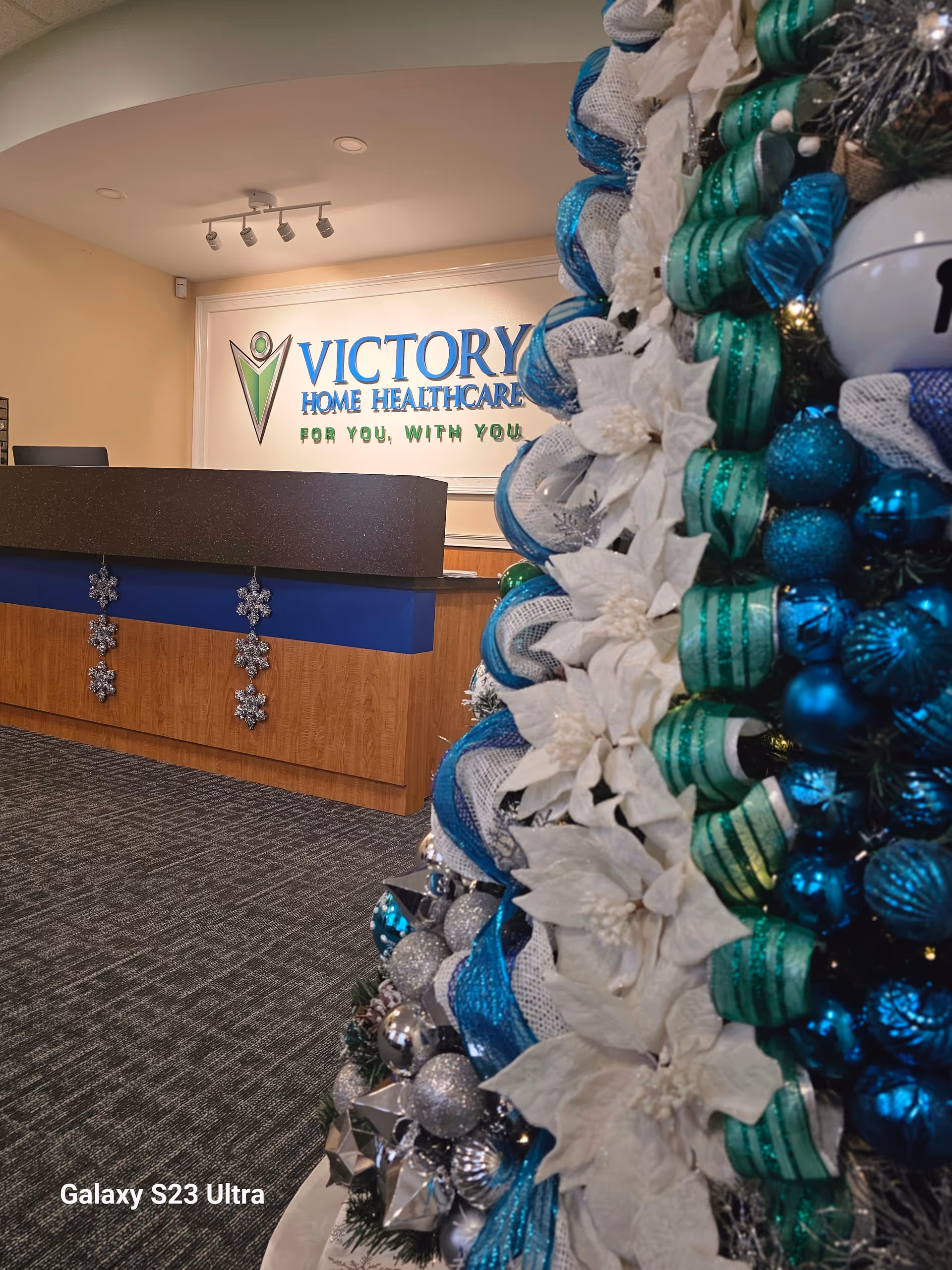 Lobby reception desk with Victory Home Healthcare sign and a festive Christmas tree in foreground.