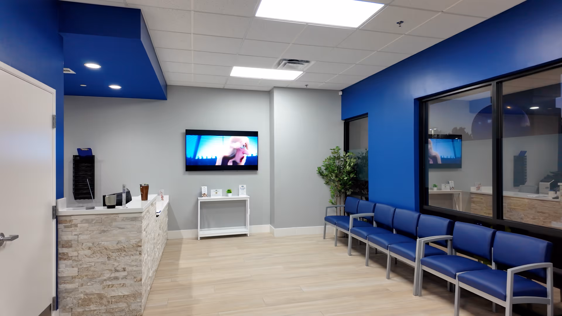 Reception area of MY DR NOW with blue walls, seating, and a wall TV.