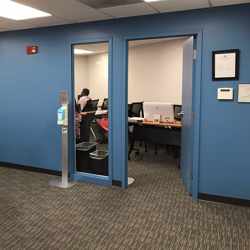 Blue-walled hallway with doorway to an office where people work at desks.