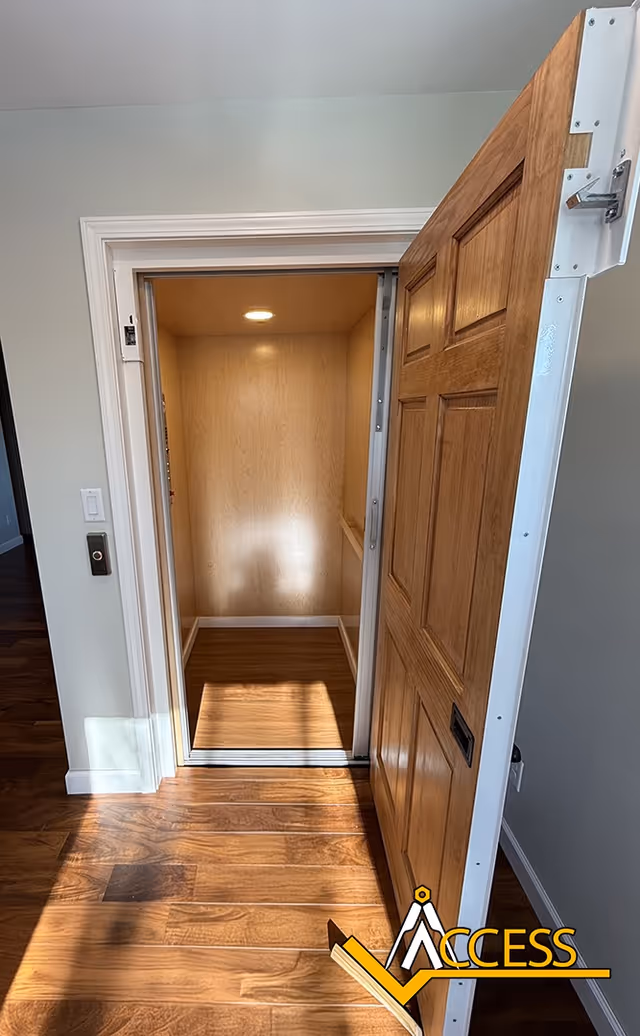 Open wooden door reveals a small elevator interior with wood walls and lighting.