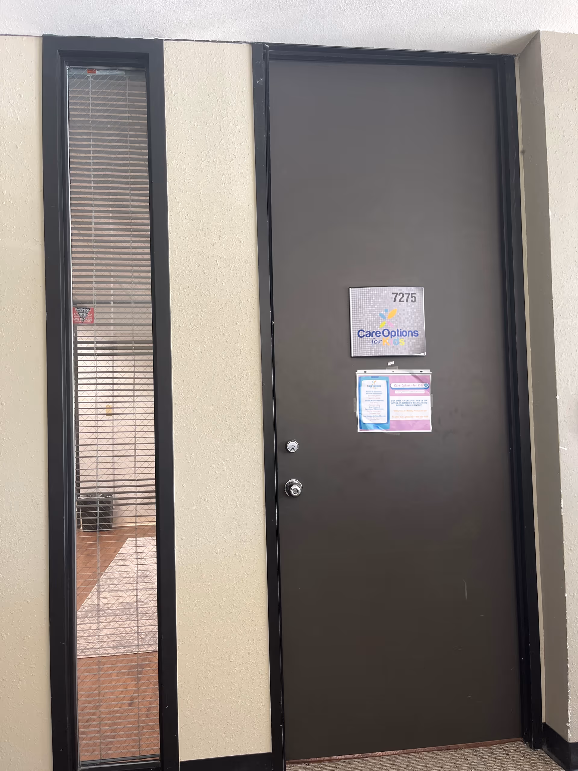Exterior door with a vertical glass panel and Care Options for Kids signs.