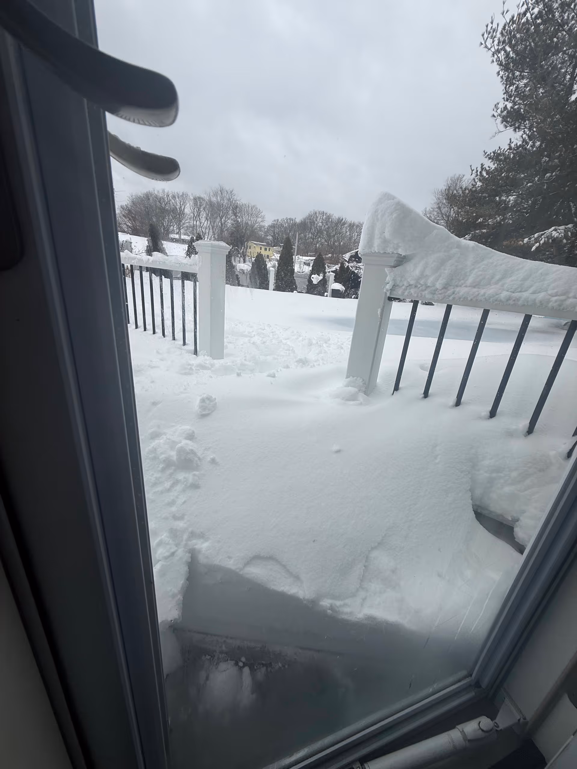 Snow blankets a balcony and yard, viewed from a doorway on a gray winter day.
