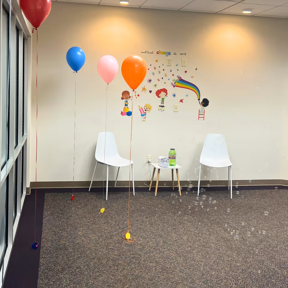 Decorated therapy room with balloons, white chairs, and a small table against a colorful wall.