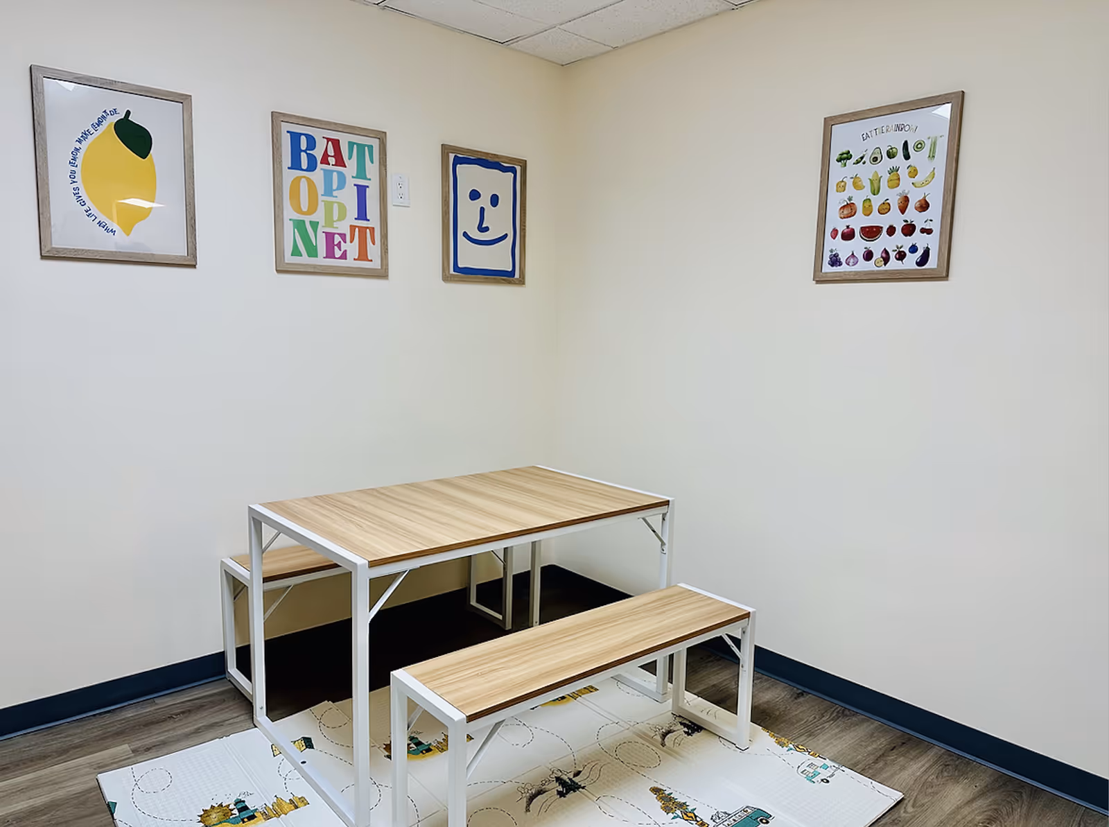 Empty therapy room with a wooden table, bench, and framed posters.