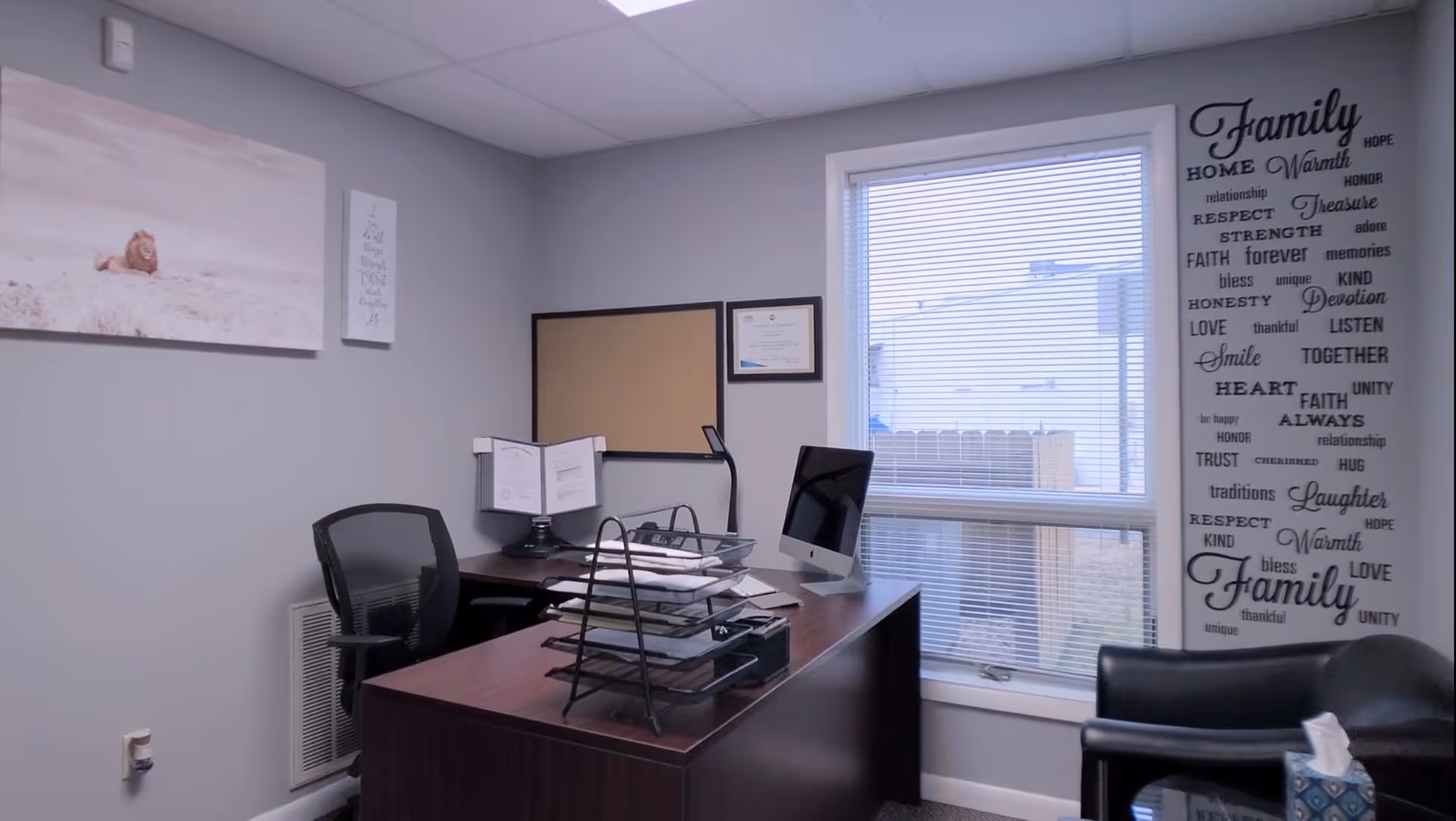 Office desk with computer, documents, and wall art in a bright room.