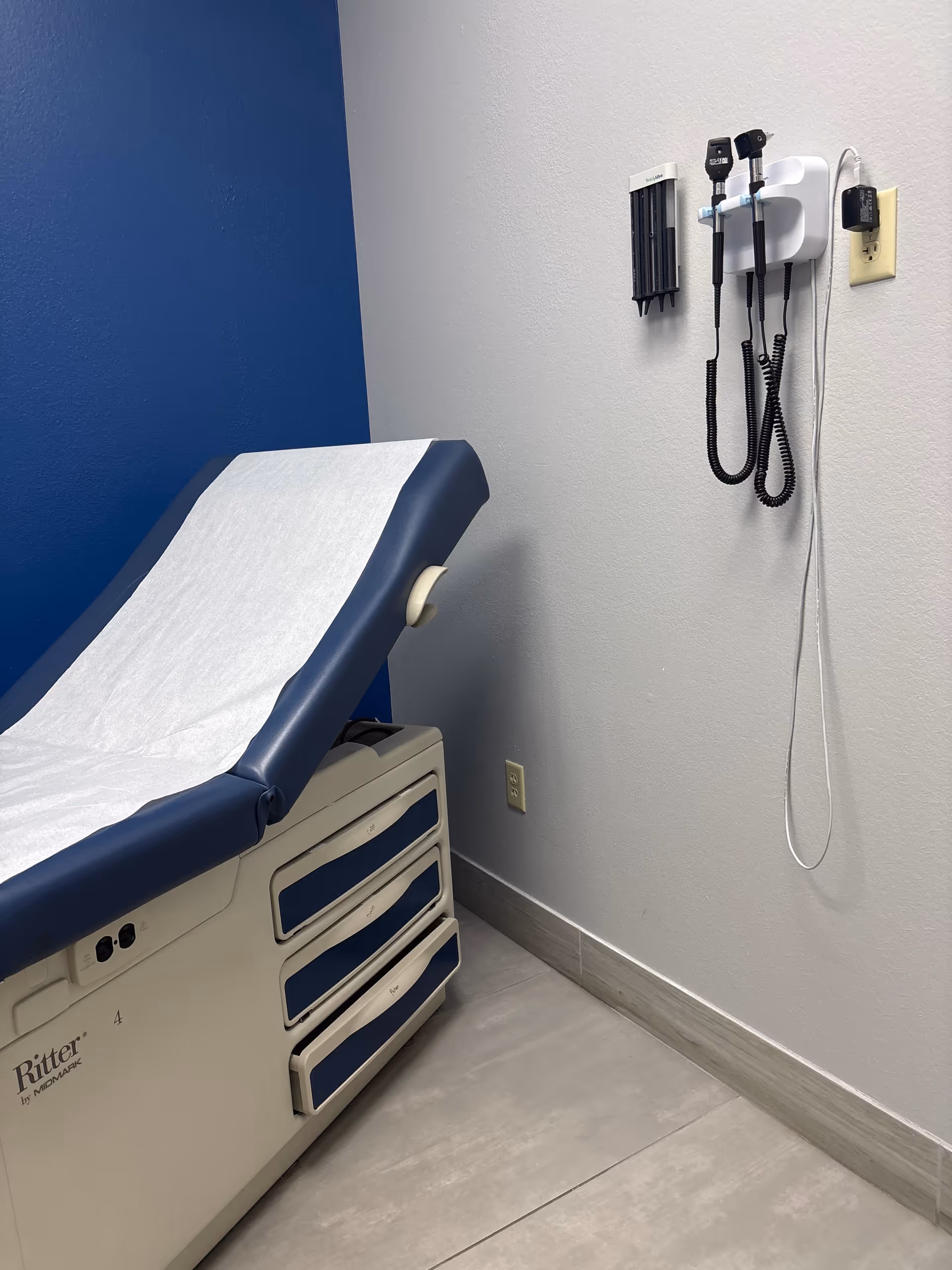 Blue examination chair with paper sheet in a small clinic room.