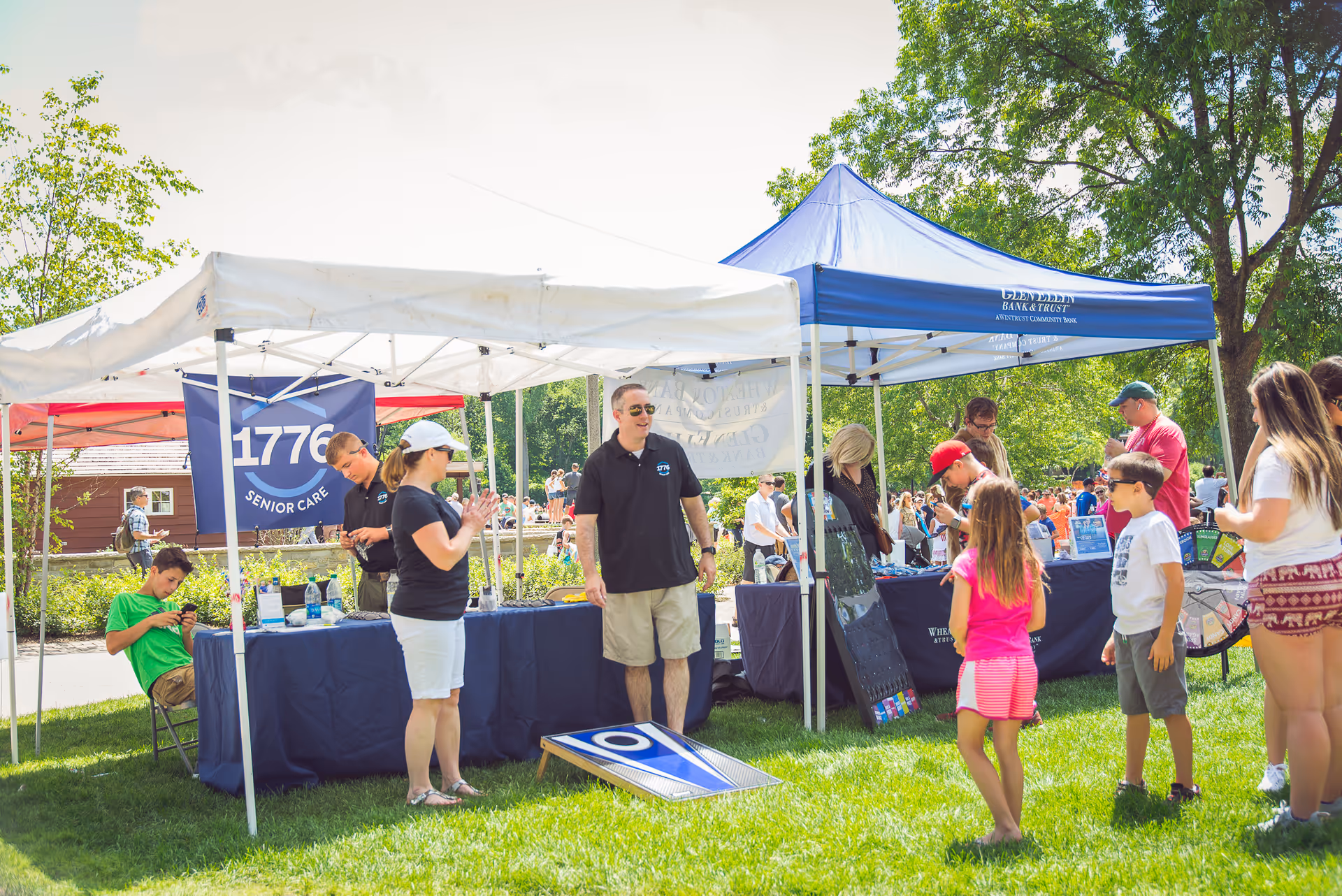 Outdoor senior-care fair with tents, booths, and attendees exploring display tables.