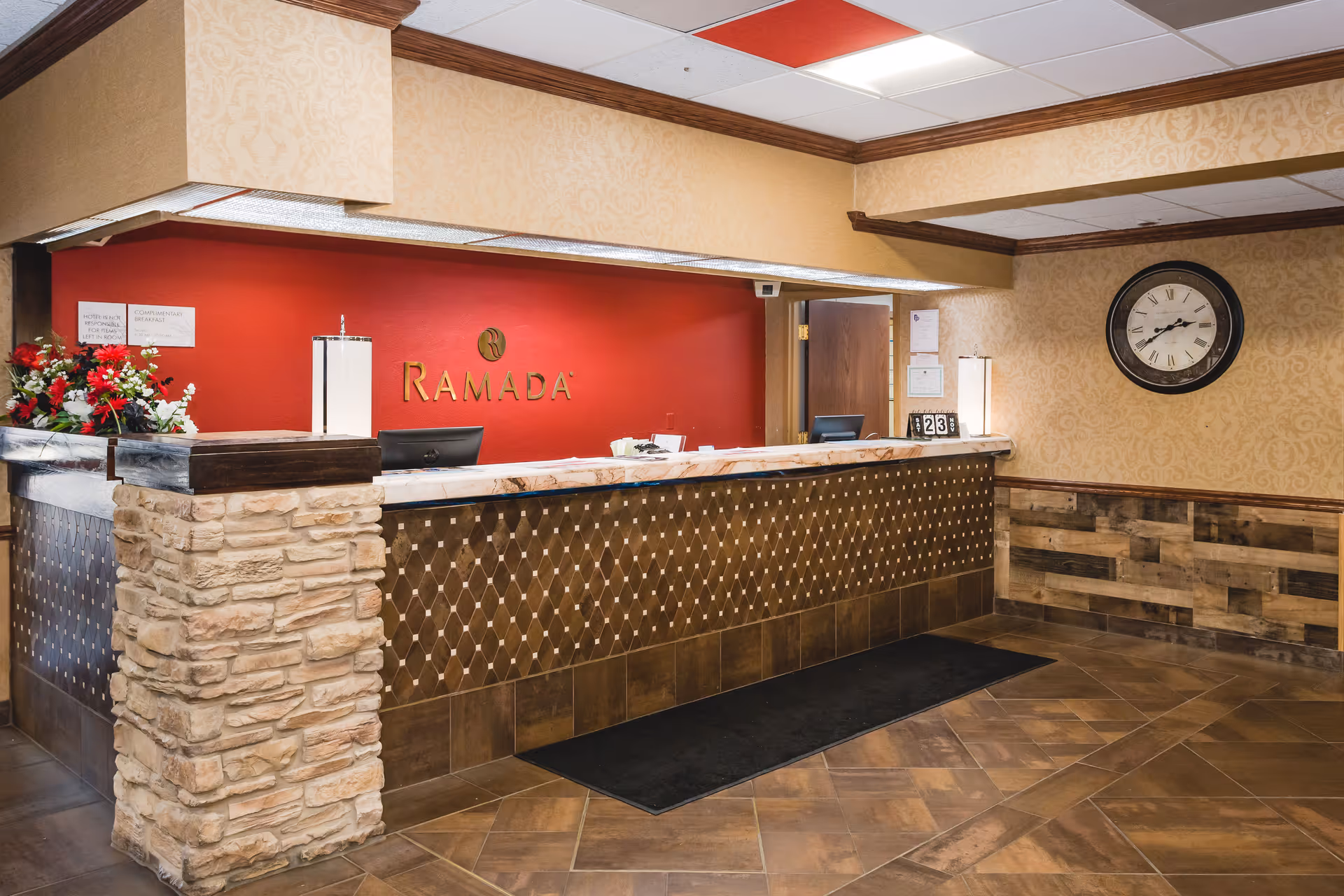 hotel-style lobby reception desk with Ramada branding, stone pillar, clock, and warm walls