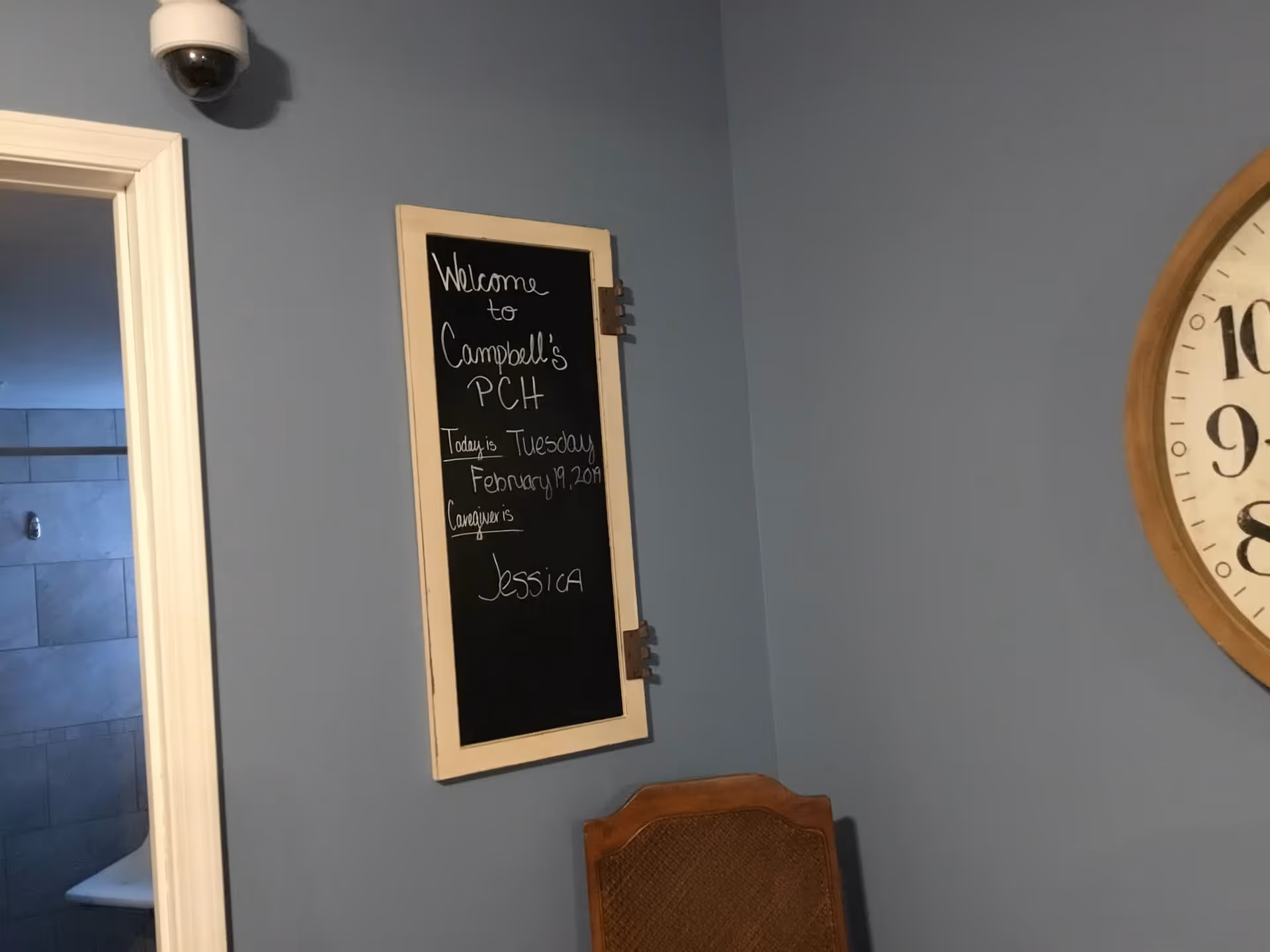 Blue interior wall with a chalkboard sign and a large clock beside a chair.