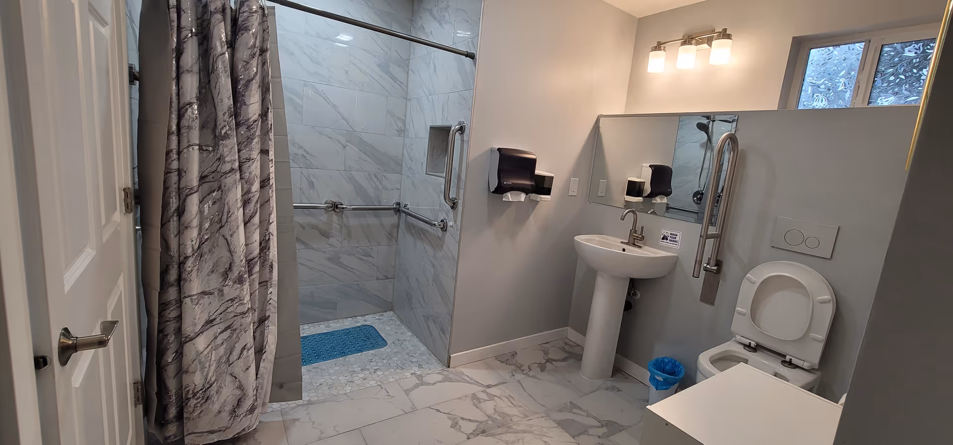 Accessible bathroom with shower, curtain, grab bars, sink, mirror, and toilet.