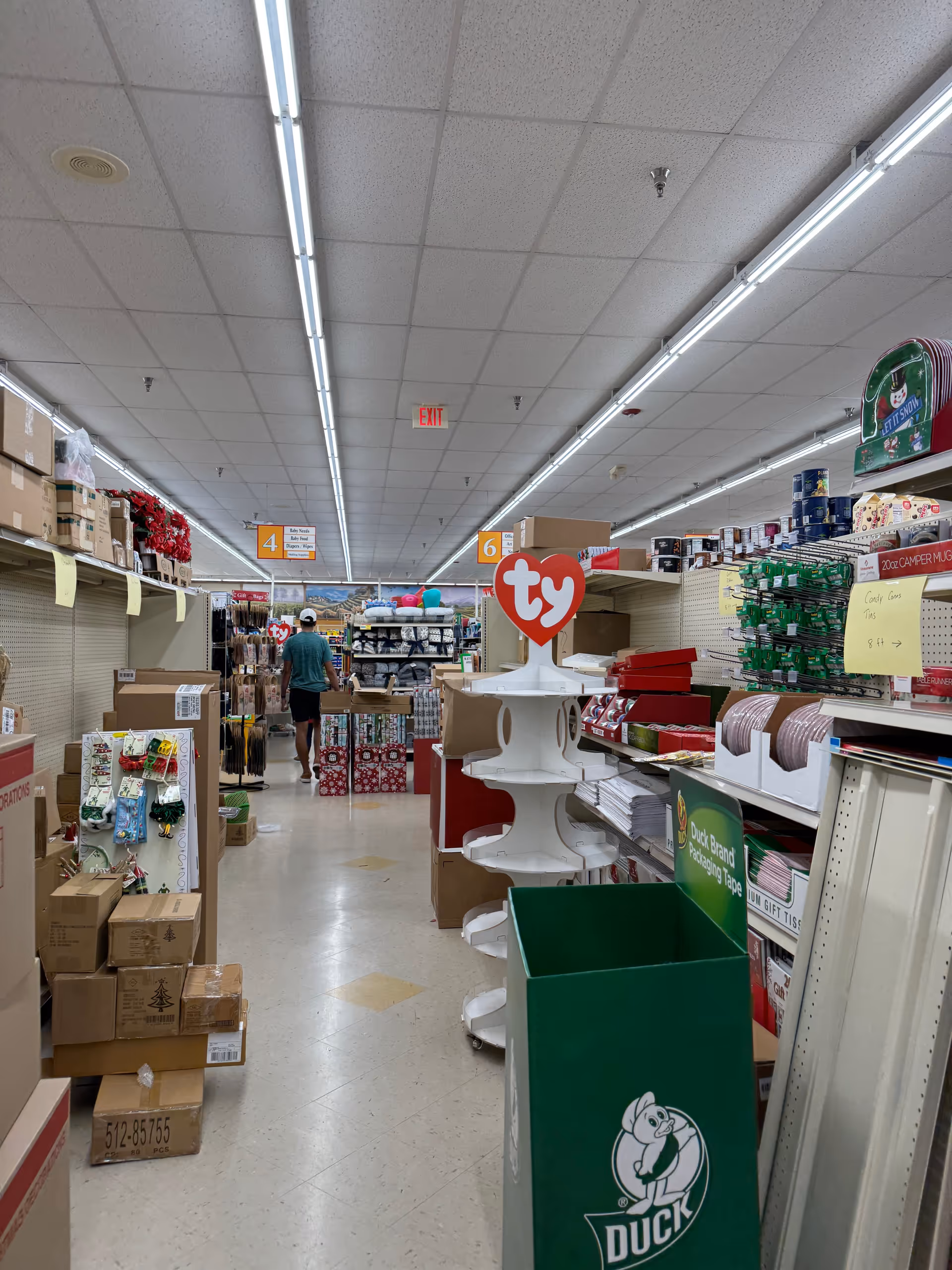 Long interior aisle at Discount Drug Mart with shelves and a shopper walking away.