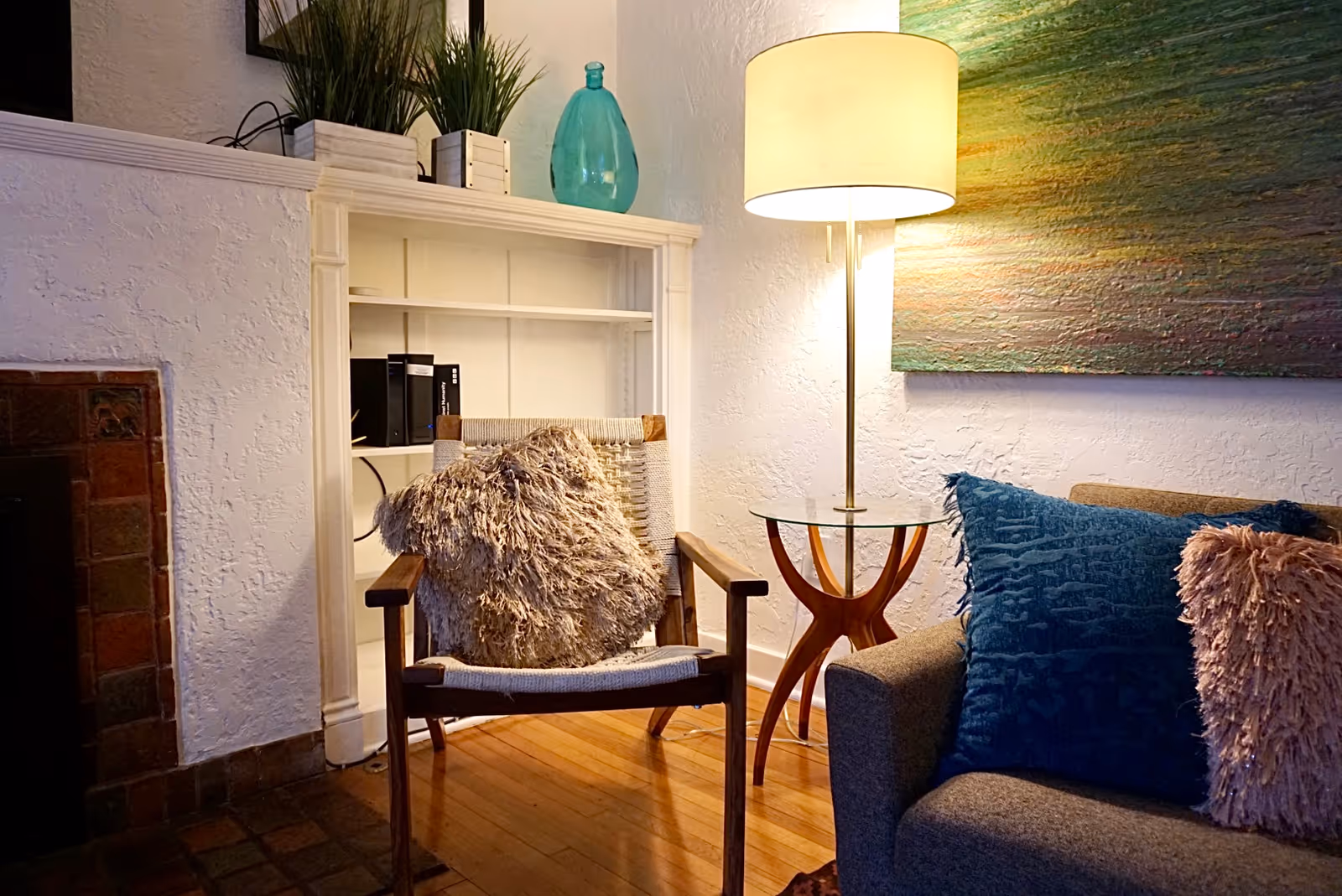 Cozy living room with chair, floor lamp, blue pillows, and a bookshelf.
