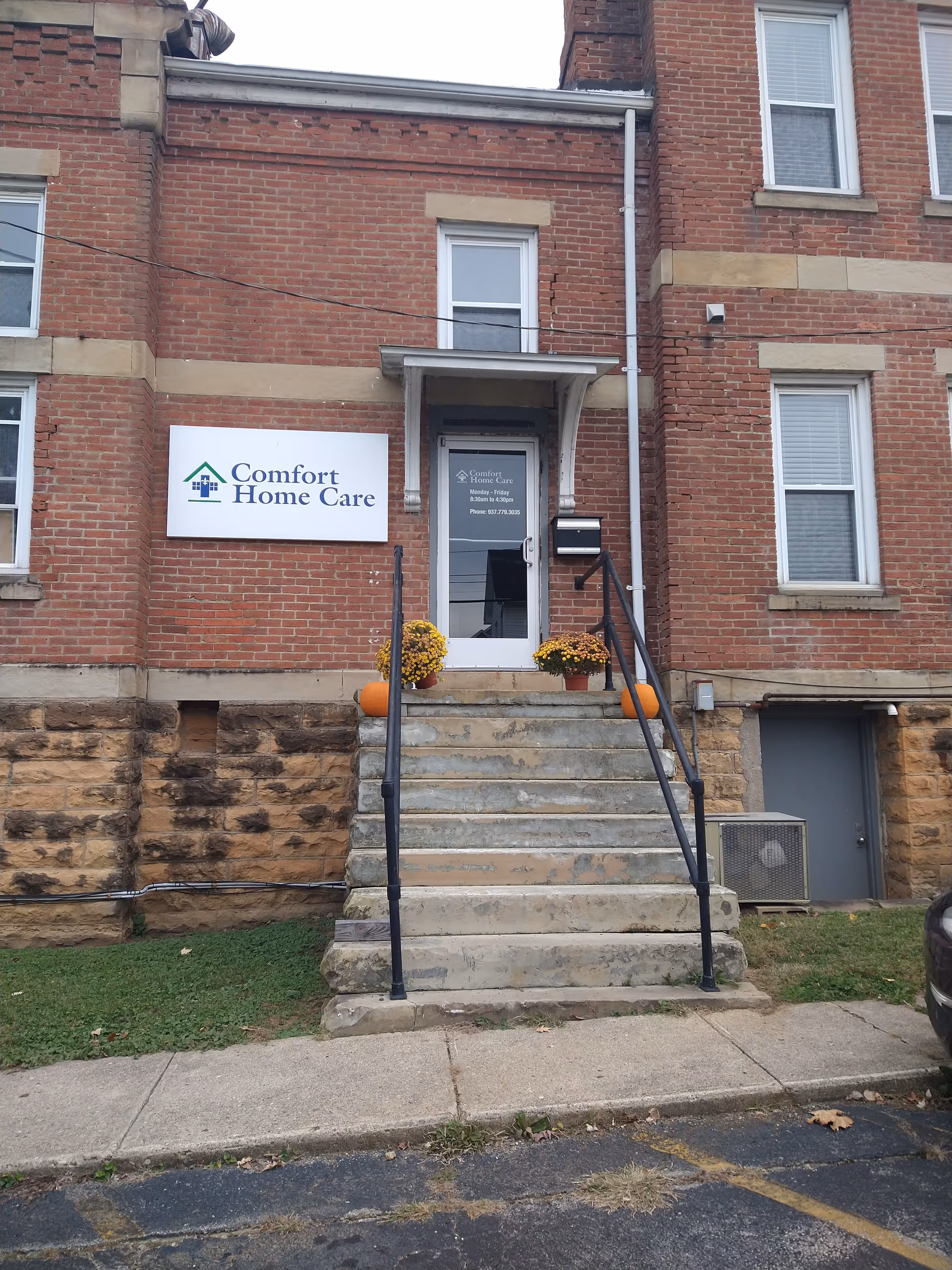 Brick senior home care building entrance with sign, steps, and pumpkins on the porch.