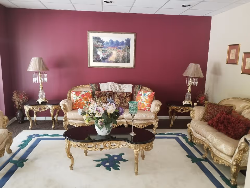 Elegant living room with ornate gold furniture, burgundy accent wall, and floral centerpiece.