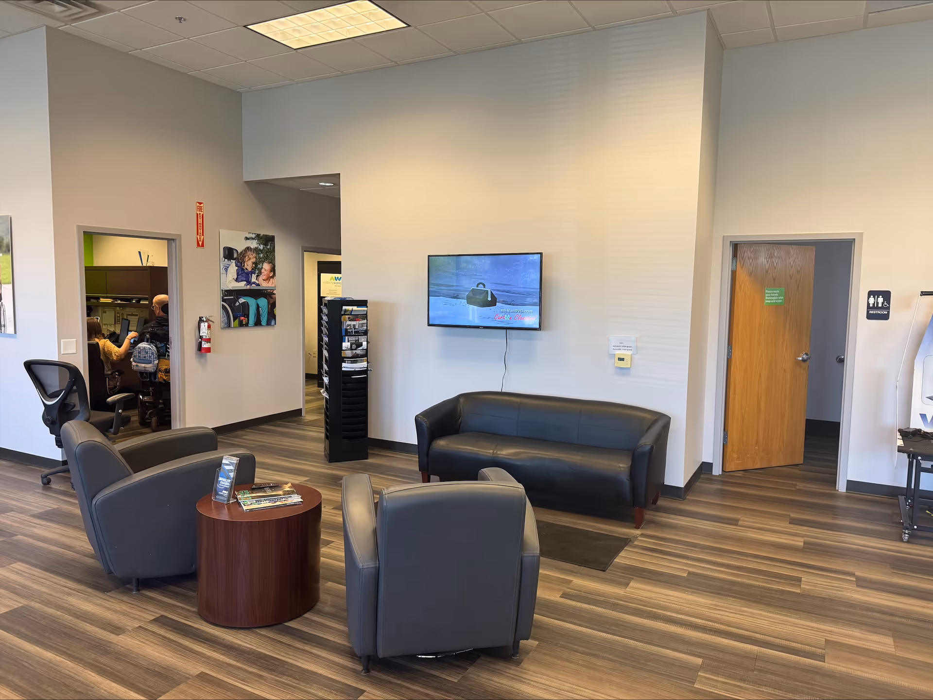A modern senior living facility lobby with seating, a wall-mounted TV, and open doorways.