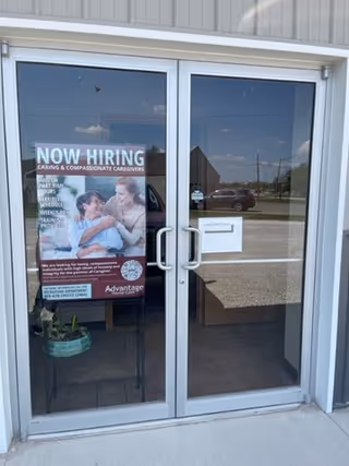 Glass double doors with a 'Now Hiring' sign and a lobby visible inside.