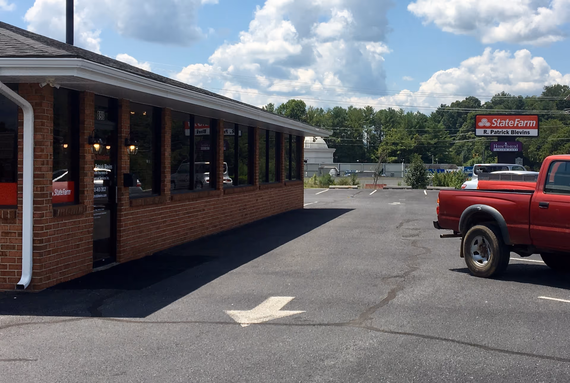 Brick building with large windows, a driveway, and a red pickup truck in the parking lot.