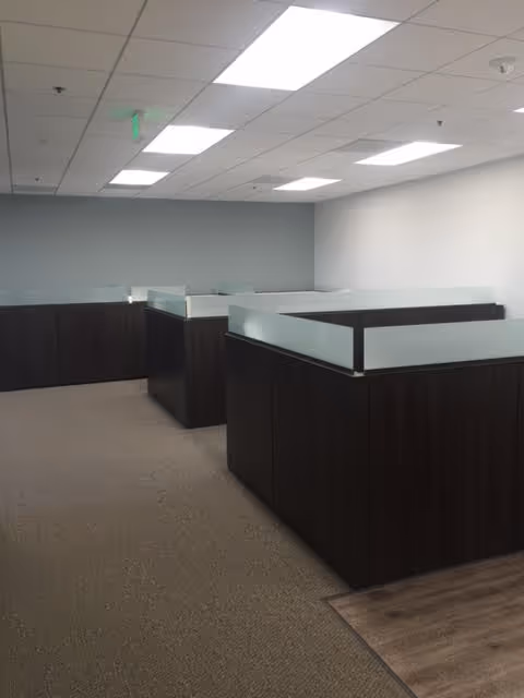 Empty office area with dark cubicles and frosted glass partitions under fluorescent lights.