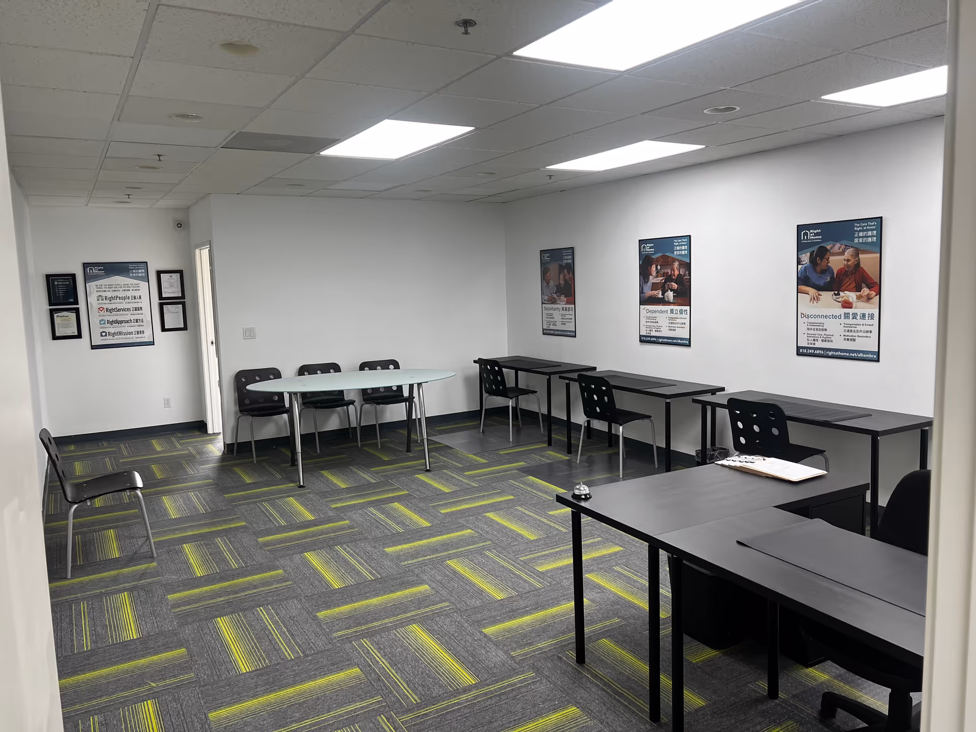 Office-style meeting room with desks along walls, scattered chairs, posters, and a patterned carpet.