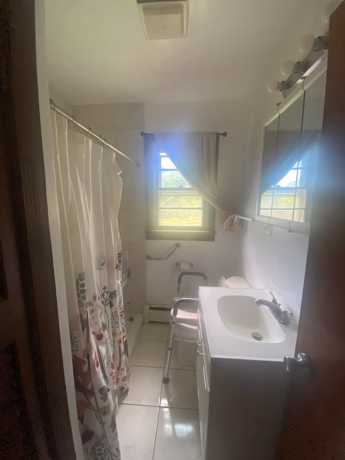 Compact bathroom with shower curtain, sink, window, and accessibility rails.