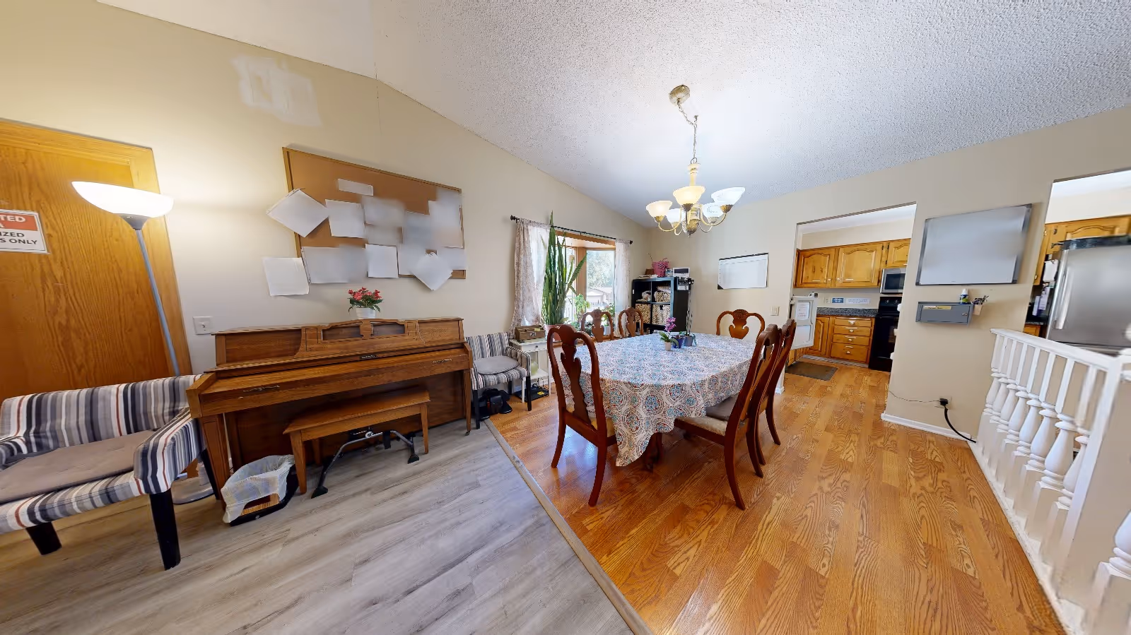 Dining room with a round table, chairs, chandelier, and kitchen visible in the background.