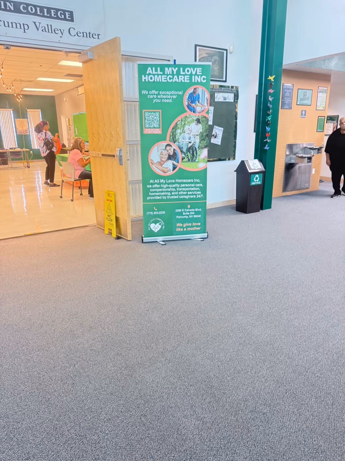 Indoor hallway of a facility with a green All My Love Homecare Inc banner and people.