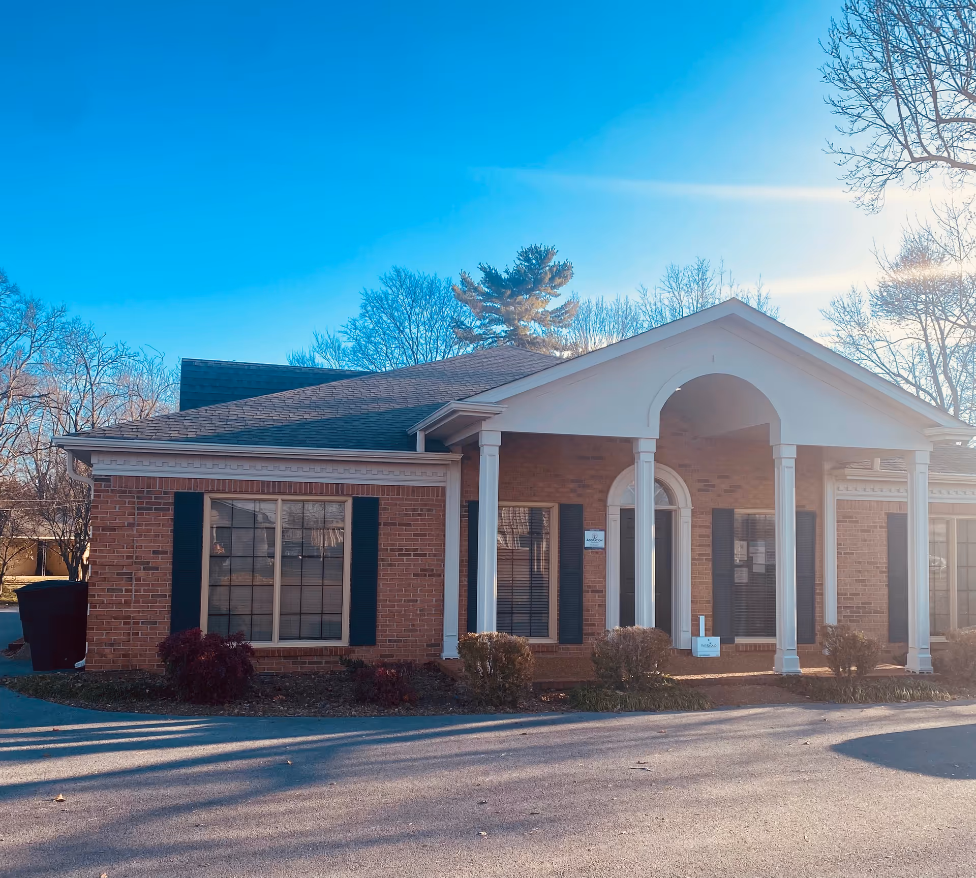 Brick facility with white columns and arched entrance under blue sky.